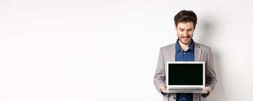 Handsome caucasian businessman in suit showing empty laptop screen, demonstrate promo, standing on white background photo