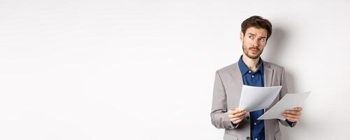 Businessman in suit looking through papers, reading documents at work and thinking, looking aside at logo, standing busy on white background photo