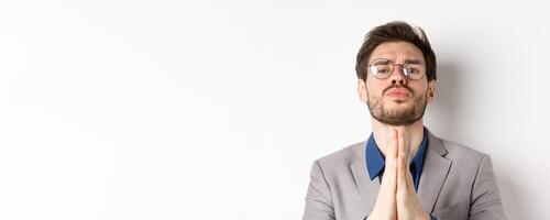 Clingy guy in glasses asking for last favour, begging for help and looking sad cute eyes, standing on white background photo