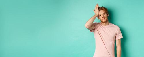 Annoyed and bothered redhead male model showing facepalm gesture, standing over mint background photo