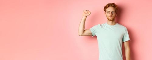 Confident redhead man standing united with black lives matter movemet, showing raised fist and looking serious at camera, protesting and being an activist, standing over pink background photo