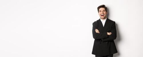 Portrait of attractive adult man in suit laughing and looking happy, standing in suit with hands crossed over chest, posing against white background photo