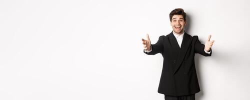 Portrait of happy attractive man in suit, hosting a party, reaching hands forward to greet you, want to hold something or hug, standing over white background photo