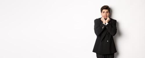 Image of scared and insecure young businessman in suit, trembling from fear and looking horrified, standing over white background photo