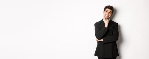 Portrait of thoughtful smiling man in stylish party suit, looking at upper left corner and thinking, imaging things, standing over white background photo