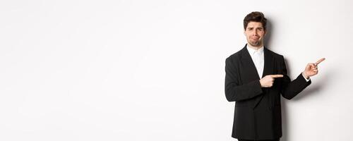 Image of devestated man in party suit, crying and complaining, pointing fingers right at something disappointing, standing over white background photo