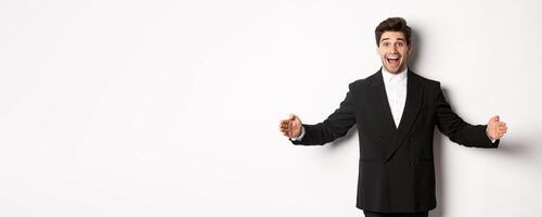 Portrait of excited handsome man in suit, shaping big object on copy space and smiling amazed, holding something, standing over white background photo