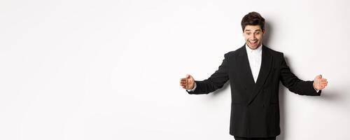Portrait of excited handsome man in suit, shaping big object on copy space and smiling amazed, holding something, standing over white background photo