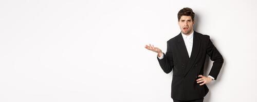 Portrait of arrogant man in black suit, looking confused and disappointed, complaining about something strange, standing over white background photo