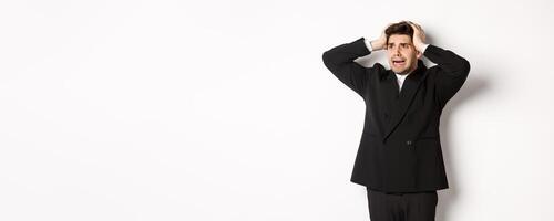 Image of anxious businessman start to panic, looking left with worried expression, standing in black suit over white background photo