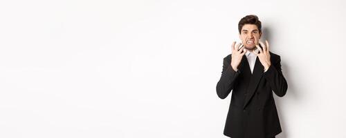 Image of angry businessman in suit, looking with furious expression and clenching fists, express hatred, standing mad over white background photo