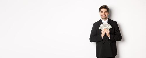 Portrait of happy and pleased handsome man in suit, hugging money and looking satisfied, standing over white background photo