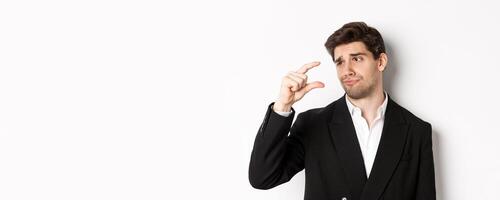 Close-up of handsome businessman in trendy suit, showing something small with disappointment, standing against white background photo