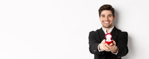 Image of handsome man looking romantic, giving you an engagement ring, making proposal to marry him, standing against white background photo