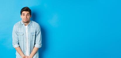 Embarrassed guy want to pee, waiting in line for toilet, standing against blue background photo