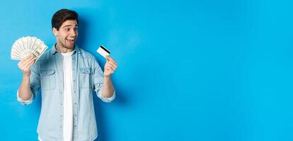 Surprised and happy man looking at credit card and showing money, concept of bank loan, finance and income. photo