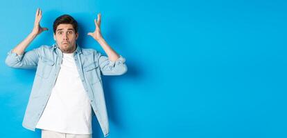 Distressed guy showing mind blowing gesture, looking frustrated and anxious, standing against blue background photo