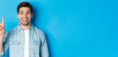 Close-up of handsome man smiling, showing fingers number two, standing over blue background photo