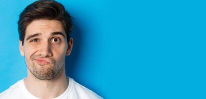 Headshot of skeptical guy looking at something unamusing, grimacing and standing reluctant against blue background photo