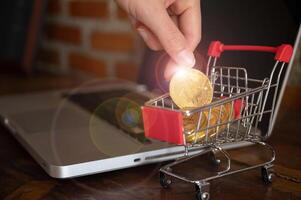 Someone hand collecting Bitcoin token in a trolley toy on laptop. Bitcoin is one of the popular cryptocurrency, a virtual currency or a digital currency. photo