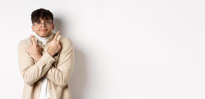 Confused funny guy in glasses pointing fingers aside, showing two variants and look indecisive, cant choose, standing on white background photo