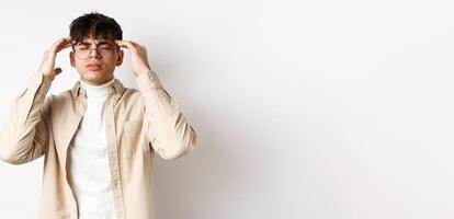 Image of young man in glasses having headache, touching head temples and frowning from painful migraine, feel dizzy, standing on white background photo