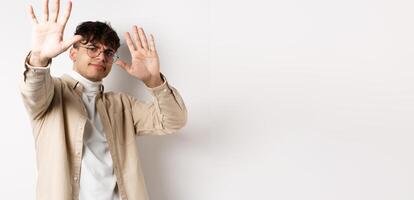 Image of reluctant and annoyed man raising hands up to block offer, refusing and asking to stop, telling no, declining something, standing on white background photo