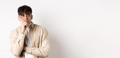 Sad and lonely young man looking at empty space with distressed face, standing thoughtful on white background photo