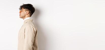 Profile of handsome caucasian man in eyewear, looking at empty space left with serious face, standing on white background photo