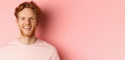 Headshot of happy redhead man with beard and white teeth, smiling excited at camera, standing over pink background photo