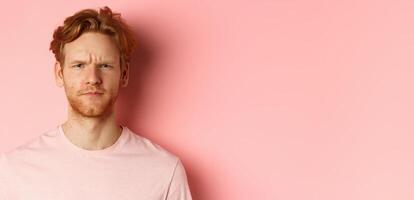 Close up of suspicious redhead guy frowning, staring at camera doubtful, express disapproval, standing over pink background photo