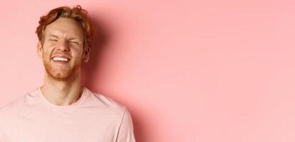 Close up of carefree man with red hair and beard, laughing and feeling happy, standing over pink background, having fun photo