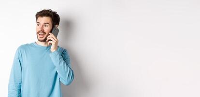 Technology concept. Cheerful man talking on mobile phone, having phone call and looking amused, standing over white background photo