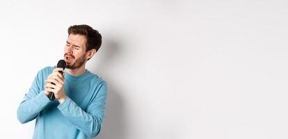 Romantic man singing song in microphone at karaoke, standing over white background photo