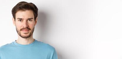 Close up of young handsome man with beard, smiling at camera with confidence, standing over white background photo