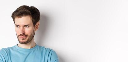 Close-up of disappointed bearded man, sulking and looking left with pensive face, standing upset over white background photo