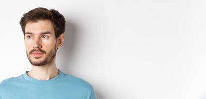 Close-up of handsome male model with beard and moustache, looking left with thoughtful face, standing over white background photo
