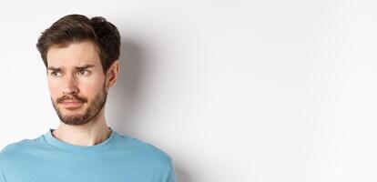 Close-up of disappointed sad man, grimacing and frowning, looking left upset, standing doubtful against white background photo