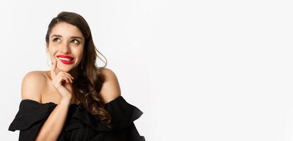 Fashion and beauty concept. Close-up of beautiful dreamy woman with red lips, looking at upper left corner and smiling tempted, having idea, standing over white background photo