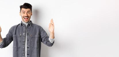 Happy guy with moustache showing big size with proud excited smile, shaping large object, standing in jacket on white background photo