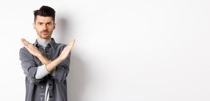 Angry man show cross gesture to stop or say no, frowning and looking serious, disagree and prohibit bad situation, standing on white background photo