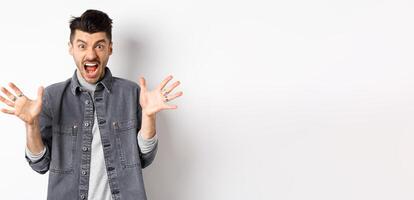 Angry man scream and look scary at camera, shouting with furious and hateful expression, standing on white background photo