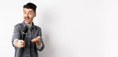 Handsome smiling man stretch out hand with microphone, giving you mic, standing on white background photo