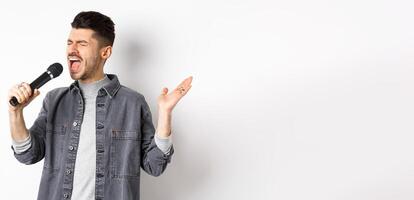 Handsome guy singing in mic with passion, perform for audience, holding microphone and gesturing, standing on white background photo