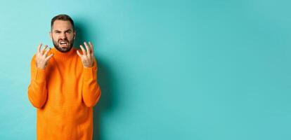 Image of angry man looking disappointed and mad, shaking hands and grimacing with disdain, standing distressed against light blue background photo