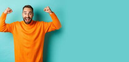 Handsome man celebrating victory, winning and looking happy, triumphing over win, standing over light blue background photo