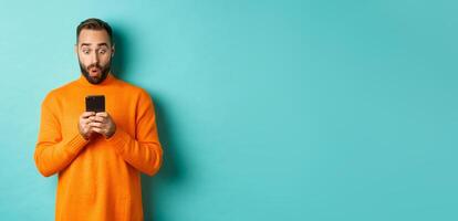 Image of man reading message with surprised face, standing amazed over light blue background photo