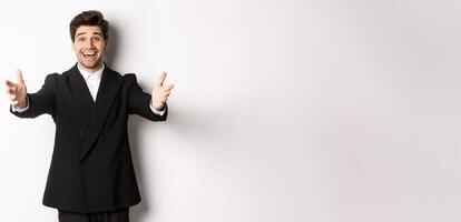 Portrait of happy attractive man in suit, hosting a party, reaching hands forward to greet you, want to hold something or hug, standing over white background photo