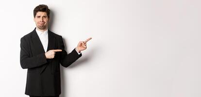 Image of devestated man in party suit, crying and complaining, pointing fingers right at something disappointing, standing over white background photo