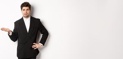 Image of confused handsome man in formal suit, raising hand and shrugging, cant understand something, standing against white background photo
